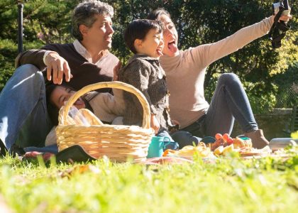 A happy family captures a selfie during a sunny picnic in a Portuguese park.